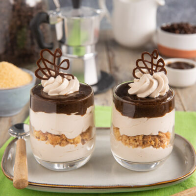 Bicchierini di yogurt al caffè a strati con biscotto sbriciolato, ciuffo di crema e decoro di cioccolato