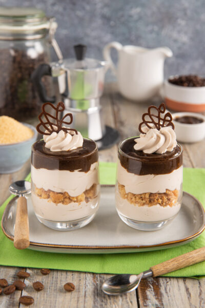 Bicchierini di yogurt al caffè a strati con biscotto sbriciolato, ciuffo di crema e decoro di cioccolato