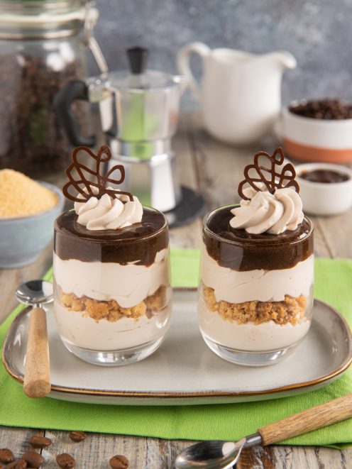 Bicchierini di yogurt al caffè a strati con biscotto sbriciolato, ciuffo di crema e decoro di cioccolato