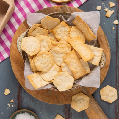 Crackers all'acqua di forme diverse in una ciotola foderata di carta forno con fiocchi di sale a lato