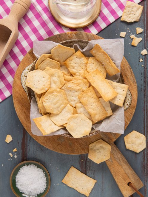 Crackers all'acqua di forme diverse in una ciotola foderata di carta forno con fiocchi di sale a lato