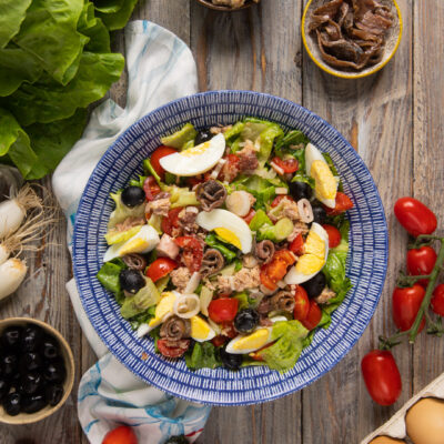 Insalata nizzarda con tonno, uova sode a spicchi, pomodorini, olive nere e acciughe arrotolate su lattuga