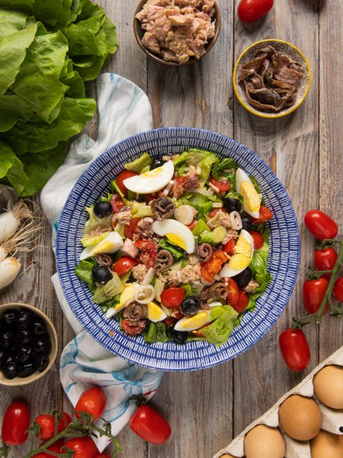 Insalata nizzarda con tonno, uova sode a spicchi, pomodorini, olive nere e acciughe arrotolate su lattuga