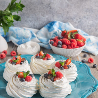 Mini pavlova classiche farcite con panna montata e guarnite con lamponi, mirtilli, fragole e menta fresca