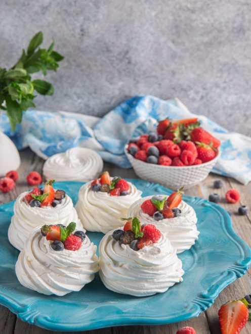Mini pavlova classiche farcite con panna montata e guarnite con lamponi, mirtilli, fragole e menta fresca