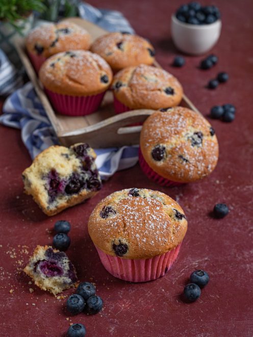 Muffin ai mirtilli spolverati di zucchero a velo, con uno aperto che mostra l'interno soffice