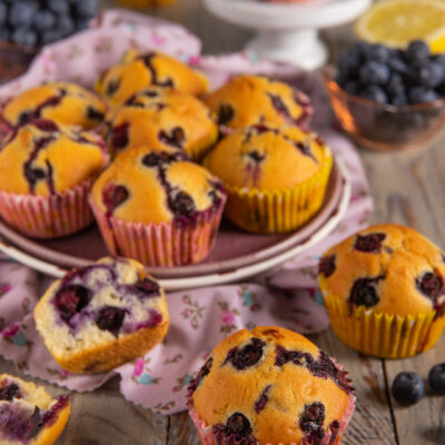 Muffin ai mirtilli senza burro con cuore soffice, serviti su tavola di legno con mirtilli freschi e limone
