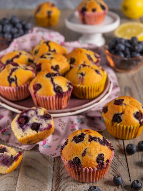 Muffin ai mirtilli senza burro con cuore soffice, serviti su tavola di legno con mirtilli freschi e limone