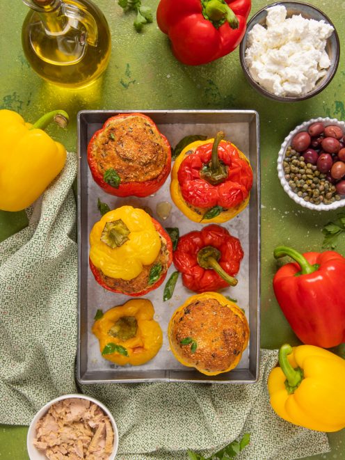Peperoni ripieni di tonno appena sfornati, rossi e gialli, con copertura gratinata e foglie di basilico