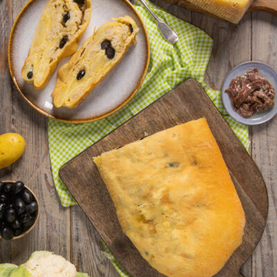 Scaccia ripiena a fette con olive nere, servita accanto al pane intero e agli ingredienti