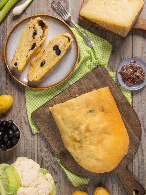 Scaccia ripiena a fette con olive nere, servita accanto al pane intero e agli ingredienti