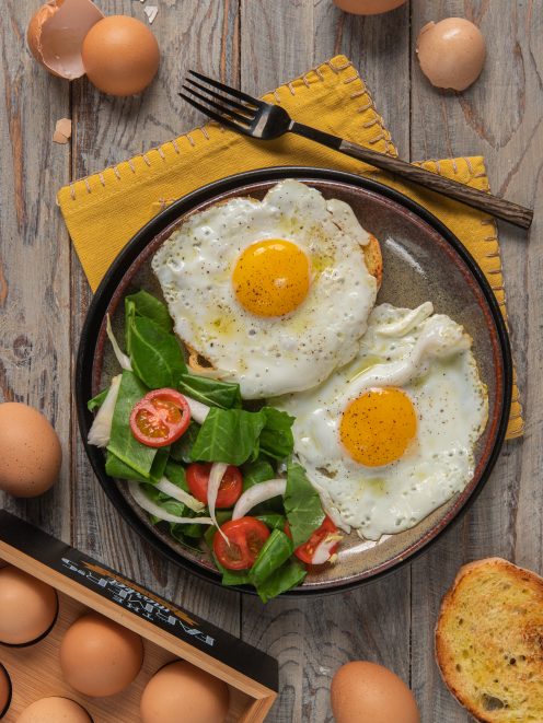 Uova all'occhio di bue con tuorlo vivace, pepe nero e insalata di spinaci e pomodorini