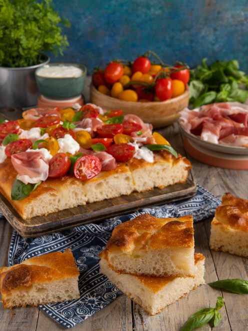 Focaccia ad alta idratazione farcita con stracciatella, pomodorini colorati, prosciutto crudo e basilico fresco