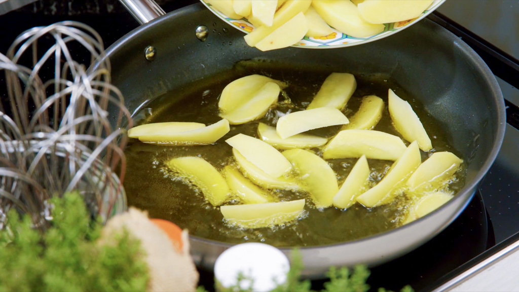 Patate che rosolano in padella con olio caldo, dorate e girate su tutti i lati