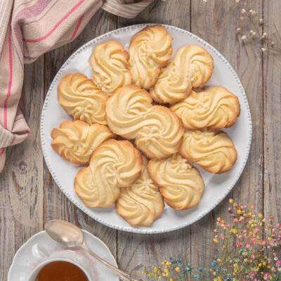 Biscotti Esse a forma di rosetta impilati su un piatto accanto a due tazze di tè