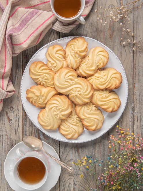 Biscotti Esse a forma di rosetta impilati su un piatto accanto a due tazze di tè