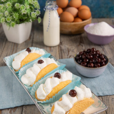 Bocche di leone farcite con panna montata e amarena sciroppata su vassoio decorato