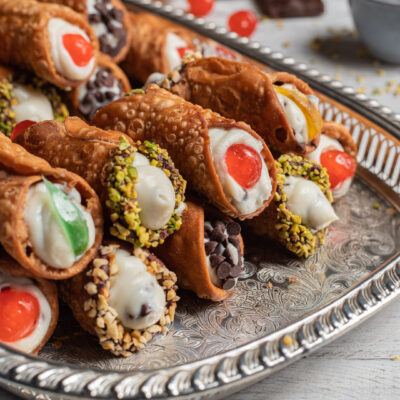 Cannoli siciliani ripieni di ricotta con granella di pistacchio, nocciole, gocce di cioccolato e ciliegie candite