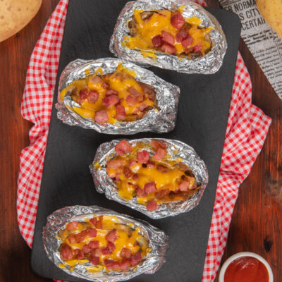 Jacket potatoes avvolte in alluminio con formaggio fuso e bacon croccante in superficie