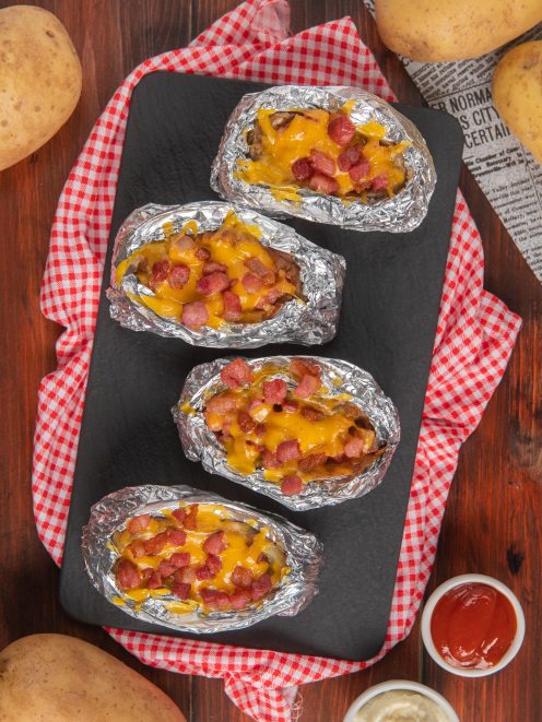 Jacket potatoes avvolte in alluminio con formaggio fuso e bacon croccante in superficie