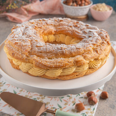 Paris Brest a corona con mandorle a lamelle, farcito di crema pralinata e spolverato di zucchero a velo