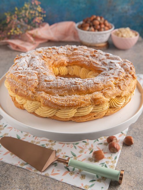 Paris Brest a corona con mandorle a lamelle, farcito di crema pralinata e spolverato di zucchero a velo