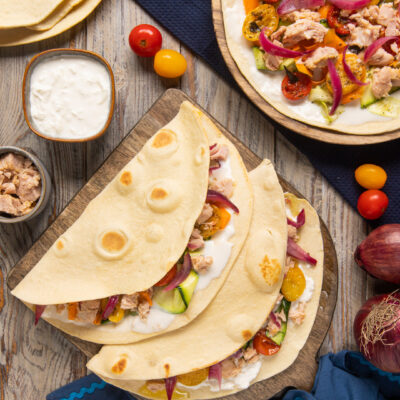 Piadine con tonno, squaquerone, zucchine, pomodorini e cipolla rossa piegate su tagliere di legno