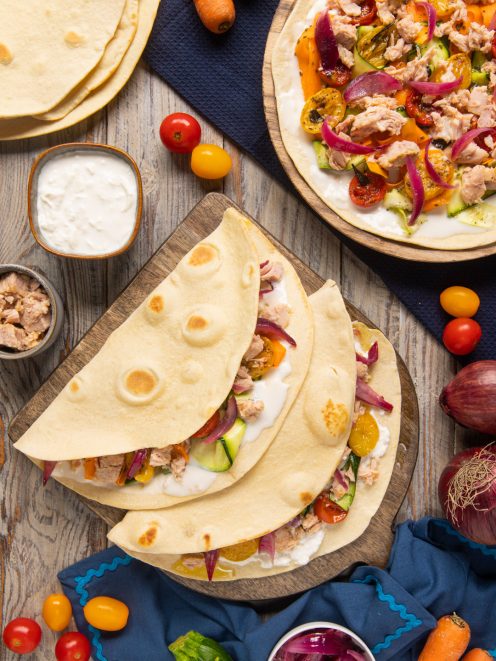 Piadine con tonno, squaquerone, zucchine, pomodorini e cipolla rossa piegate su tagliere di legno