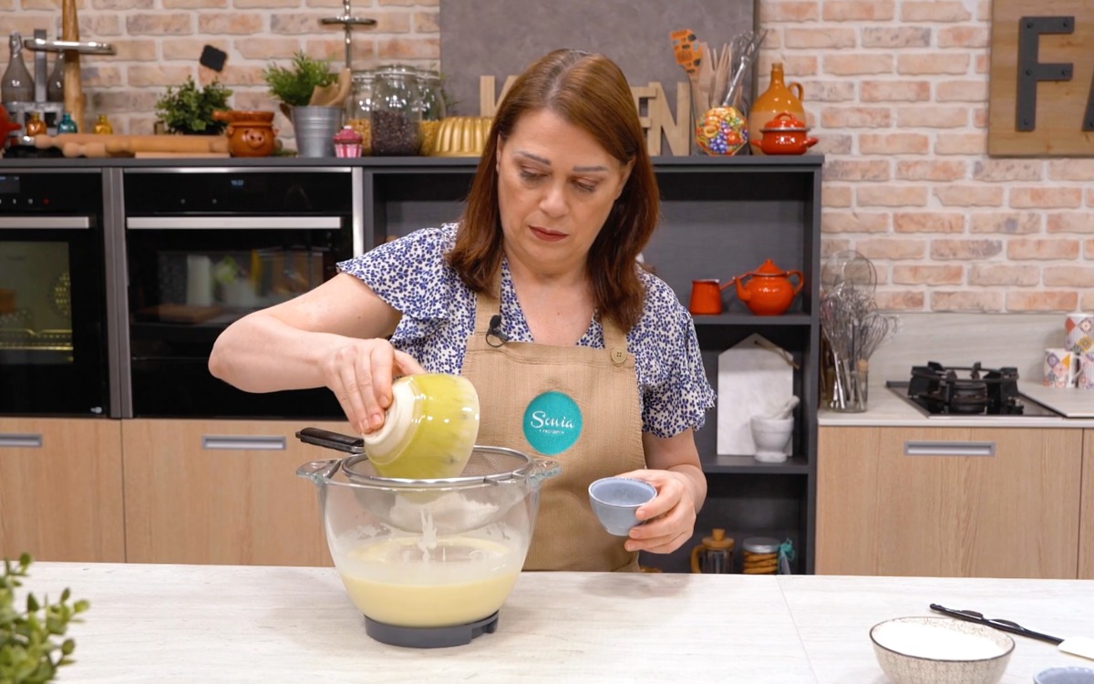 Una cuoca versa olio a filo nella planetaria mentre monta il composto per la torta al cocco