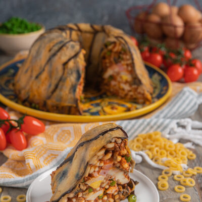 Anelletti alla siciliana in forma a cupola rivestita di melanzane, con una fetta tagliata che rivela il ripieno