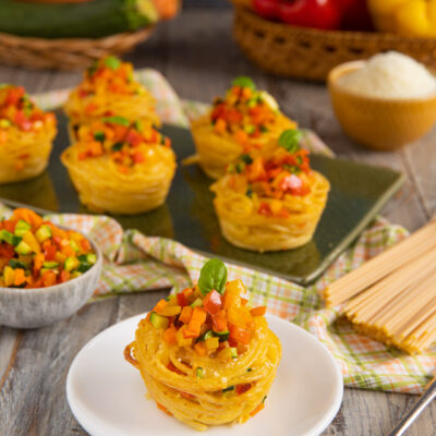 Cupcake di spaghetti nido con dadolata di peperoni, zucchine e carote e foglia di basilico