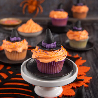 Cupcake stregati con glassa arancione, sprinkle colorati e cappello da strega in pasta di zucchero
