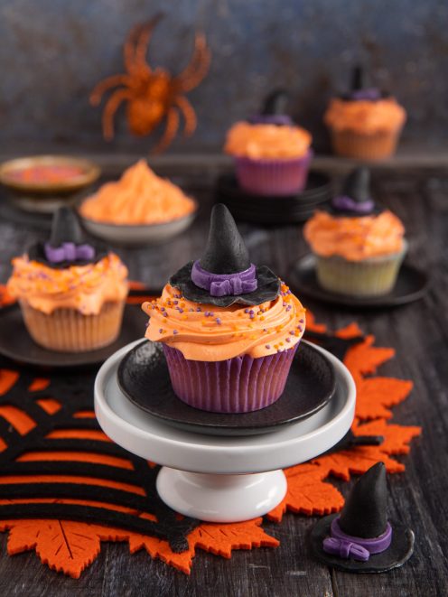 Cupcake stregati con glassa arancione, sprinkle colorati e cappello da strega in pasta di zucchero