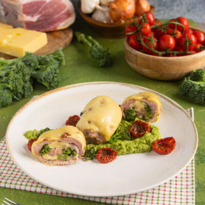 Involtini di carne ripieni di broccoletti, gratinati con formaggio fuso su crema verde e pomodorini secchi