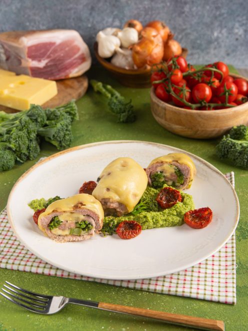 Involtini di carne ripieni di broccoletti, gratinati con formaggio fuso su crema verde e pomodorini secchi