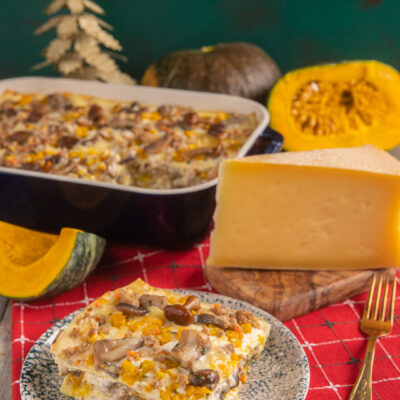 Lasagne con ragù bianco, zucca e funghi impilate a strati e servite con una fetta di formaggio stagionato