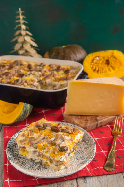 Lasagne con ragù bianco, zucca e funghi impilate a strati e servite con una fetta di formaggio stagionato