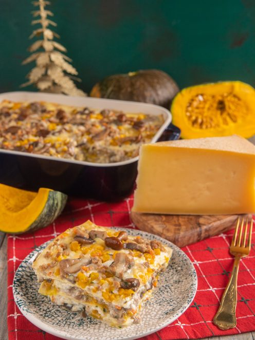 Lasagne con ragù bianco, zucca e funghi impilate a strati e servite con una fetta di formaggio stagionato