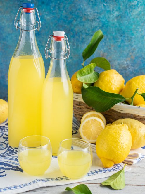 Limoncello fatto in casa in due bottiglie con limoni freschi con foglie accanto