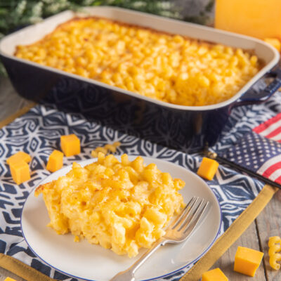 Maccheroni cheese gratinati al forno serviti in porzione con cubetti di cheddar e teglia sullo sfondo