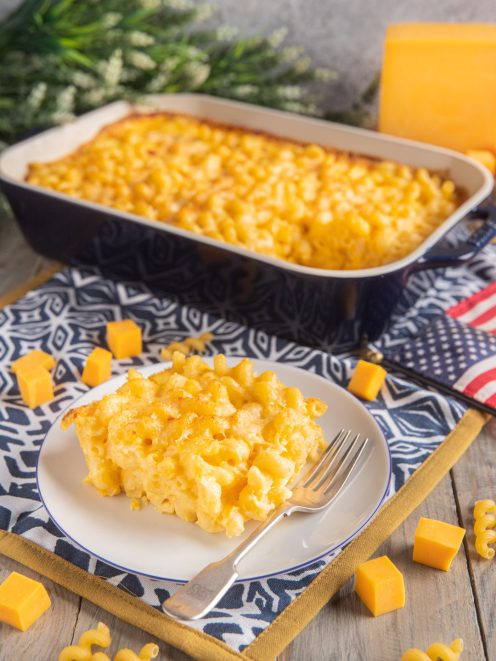 Maccheroni cheese gratinati al forno serviti in porzione con cubetti di cheddar e teglia sullo sfondo