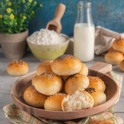 Panini al latte soffici impilati, alcuni con semi di sesamo e papavero, uno spezzato a metà