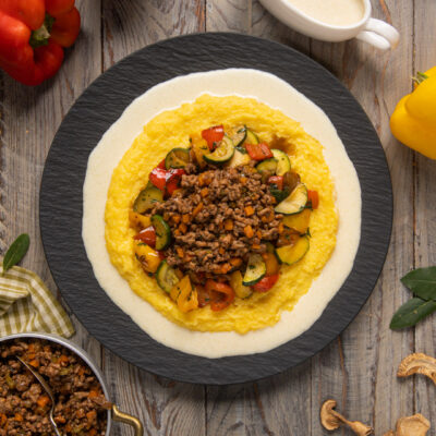 Polenta con ragù bianco e crema di parmigiano guarnita con verdure a dadini colorate