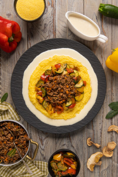 Polenta con ragù bianco e crema di parmigiano guarnita con verdure a dadini colorate