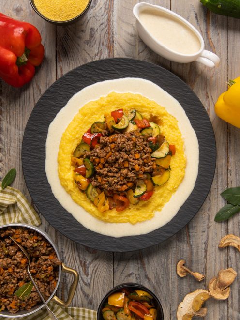 Polenta con ragù bianco e crema di parmigiano guarnita con verdure a dadini colorate