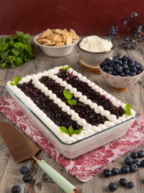 Tiramisù allo yogurt e mirtilli decorato con ciuffi di panna e foglioline di menta fresca