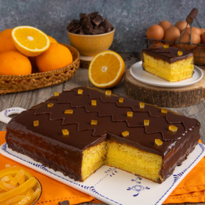 Torta arancia e cioccolato con glassa lucida e cubetti di scorza candita, una fetta tagliata rivela il pan di spagna soffice