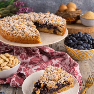 Torta soffice con crumble ai mirtilli tagliata a fette, con farcitura ai frutti di bosco e zucchero a velo