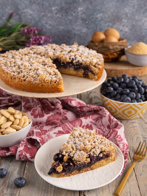 Torta soffice con crumble ai mirtilli tagliata a fette, con farcitura ai frutti di bosco e zucchero a velo