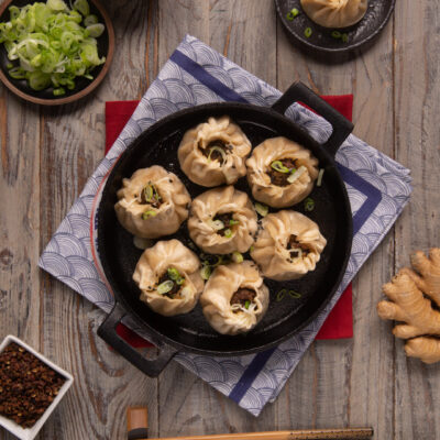 Baozi con manzo e cipolle in padella di ferro, guarniti con cipollotto fresco e sesamo nero